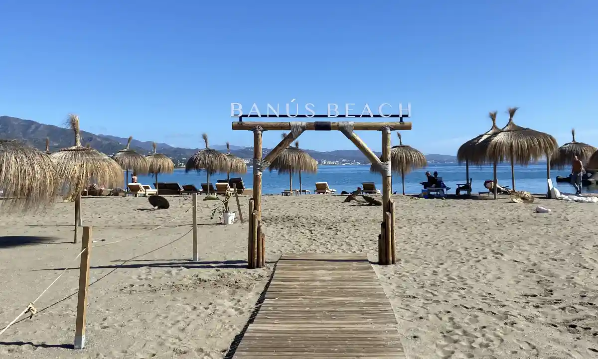 Puerto Banús Beach with iconic beach sign, parasols and beautiful blue water