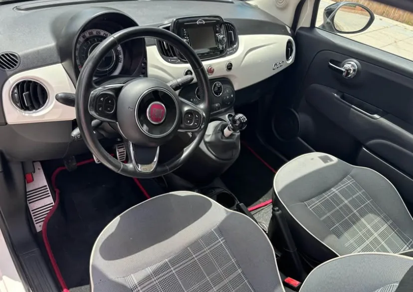 Interior view of a Fiat 500 in Marbella, showing its stylish dashboard with a retro-modern design, multifunction steering wheel, manual gear shift, touchscreen display, and comfortable plaid-patterned seats. The clean and compact cabin highlights why travelers looking to rent a Fiat 500 in Marbella appreciate its charm, ease of driving, and practical layout for navigating the streets of the Costa del Sol.