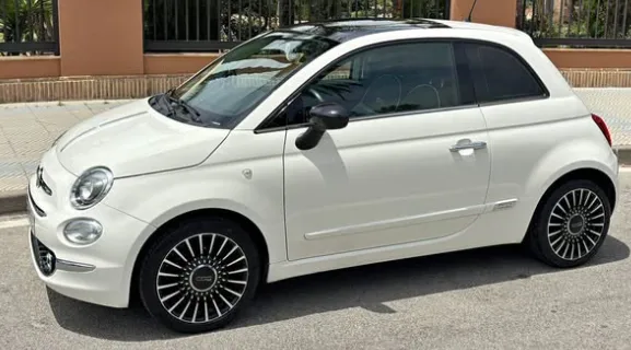 A white Fiat 500 parked on a sunny street in Marbella, showcasing its iconic compact design, rounded headlights, stylish black roof, and modern alloy wheels. This small and fuel-efficient city car is perfect for travelers looking to rent a Fiat 500 in Marbella, offering easy parking, excellent maneuverability, and a charming retro look while exploring the Costa del Sol. The bright urban setting enhances its appeal for anyone searching to rent a car in Marbella.