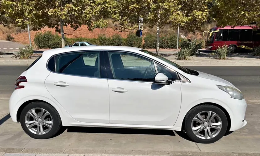 A white Peugeot 208 parked on a sunny street in Marbella, showing its compact hatchback design, clean body lines, and modern alloy wheels. This well-maintained car is ideal for travelers looking to rent a Peugeot 208 in Marbella, offering a practical, fuel-efficient, and comfortable option for exploring the Costa del Sol. The bright urban surroundings reinforce the convenience and value of choosing this model when searching to rent a car in Marbella.