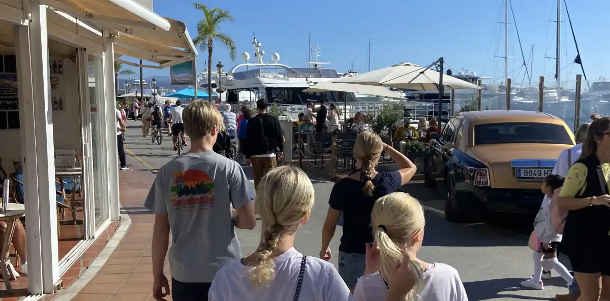 Families walking along Puerto Banús waterfront with luxury superyachts in background, restaurants and shops lining the promenade – popular tourist destination near Marbella