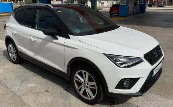 A white Seat Arona parked at a fuel station in Marbella, highlighting its compact SUV design, sharp LED headlights, sporty alloy wheels, and modern black roof accents. This versatile and fuel-efficient crossover is ideal for travelers looking to rent a Seat Arona in Marbella, offering comfort, practicality, and a higher driving position for exploring the Costa del Sol. The bright outdoor setting reinforces its appeal for anyone searching to rent a car in Marbella.